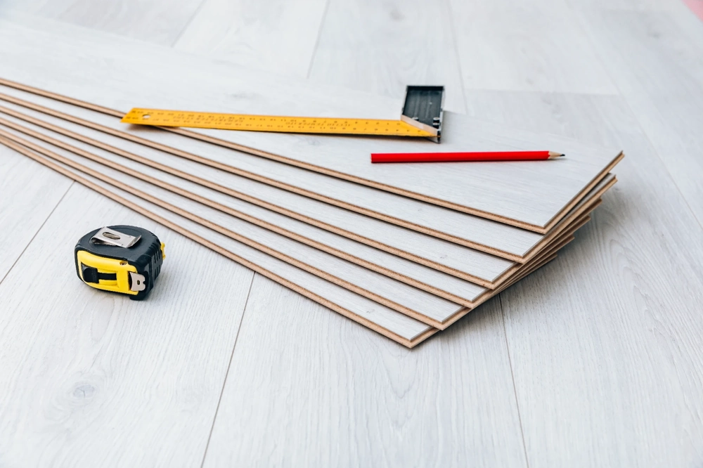 Parquet flottant : planches empilées sur sol clair avec mètre ruban, équerre et crayon de marquage