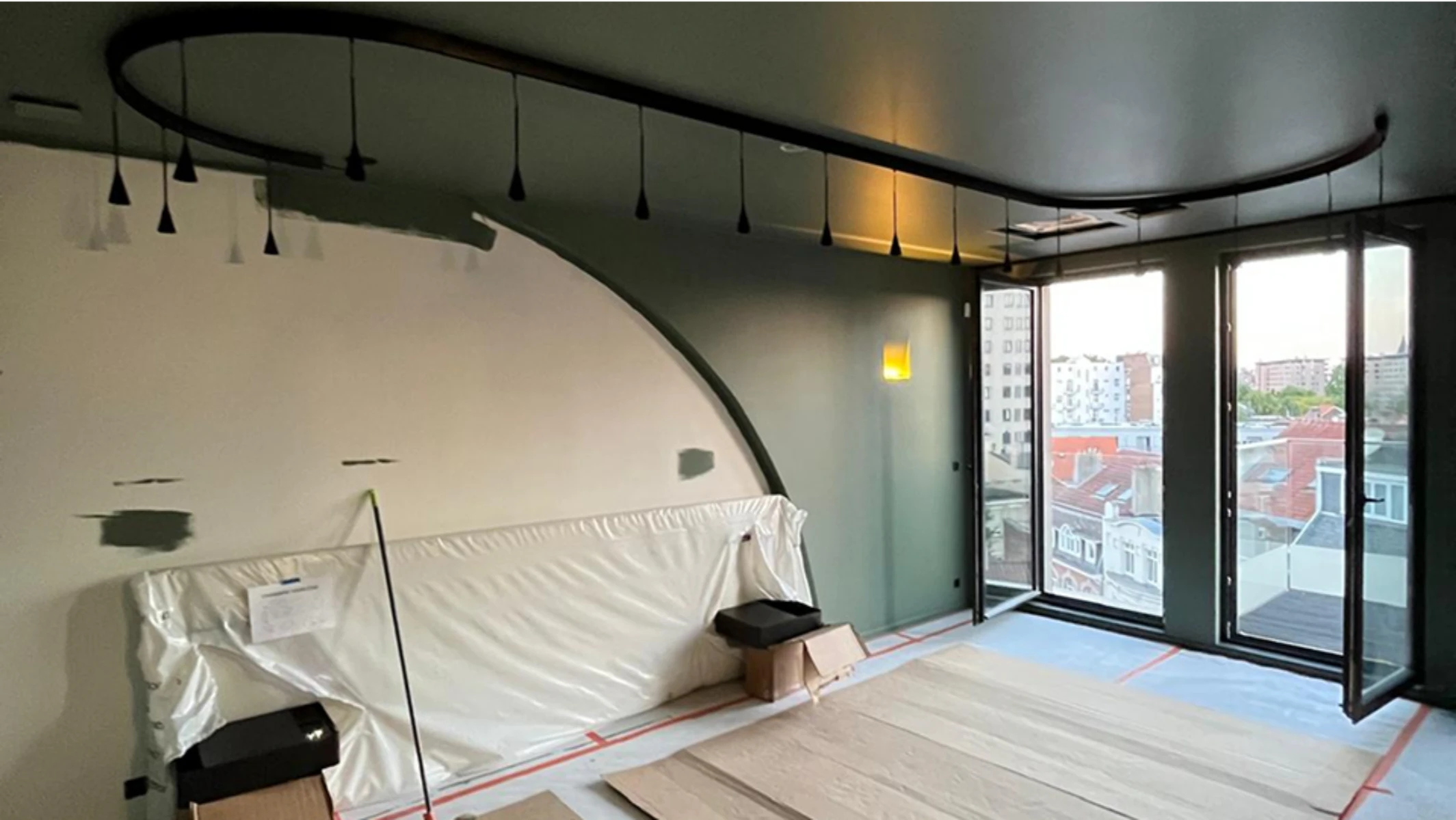 Salon en cours de finition avec faux plafond courbe et luminaires LED suspendus, sol protégé