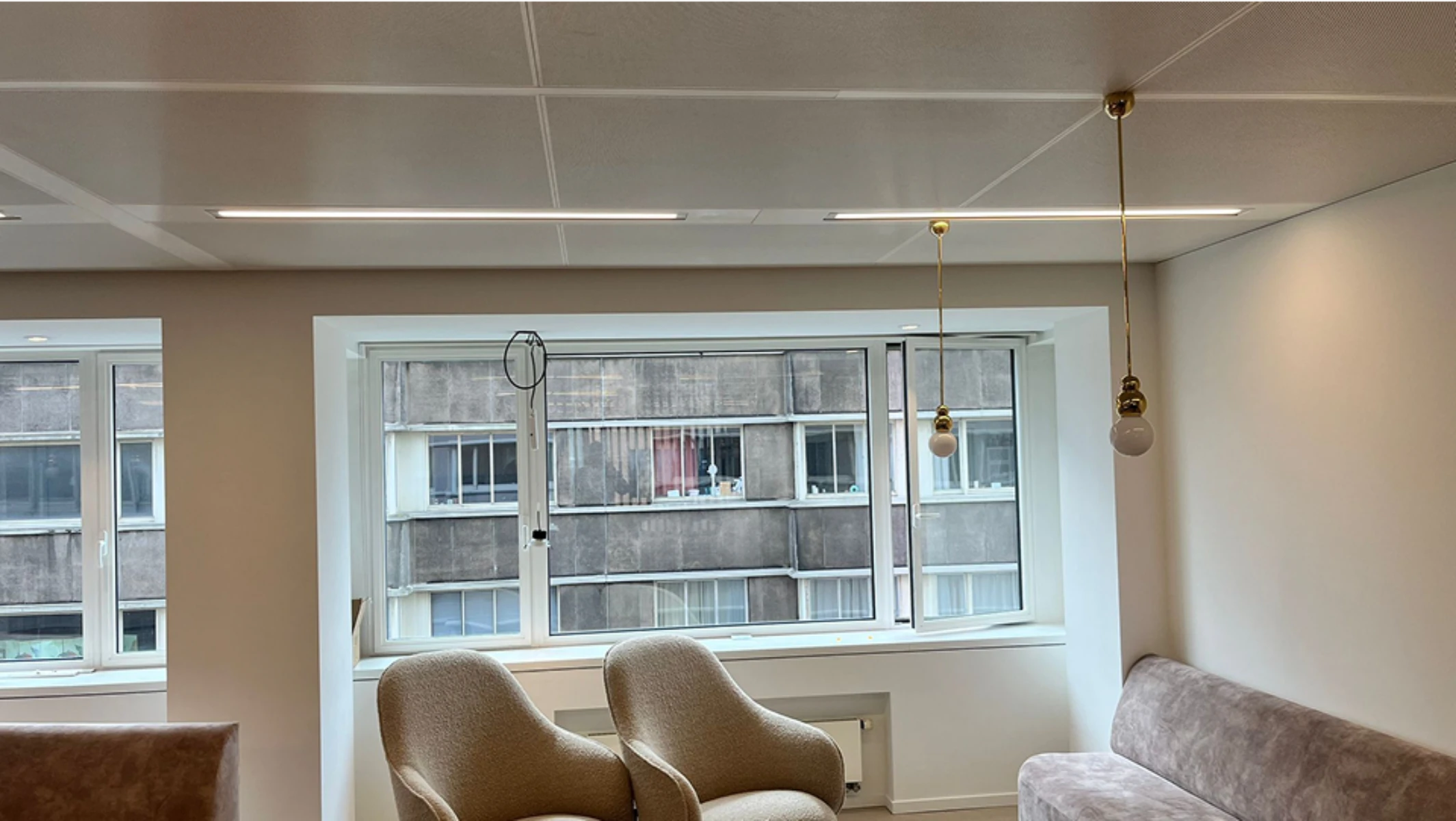 Intérieur rénové avec faux plafond, éclairage LED et suspensions, deux fauteuils et un canapé dans un salon moderne