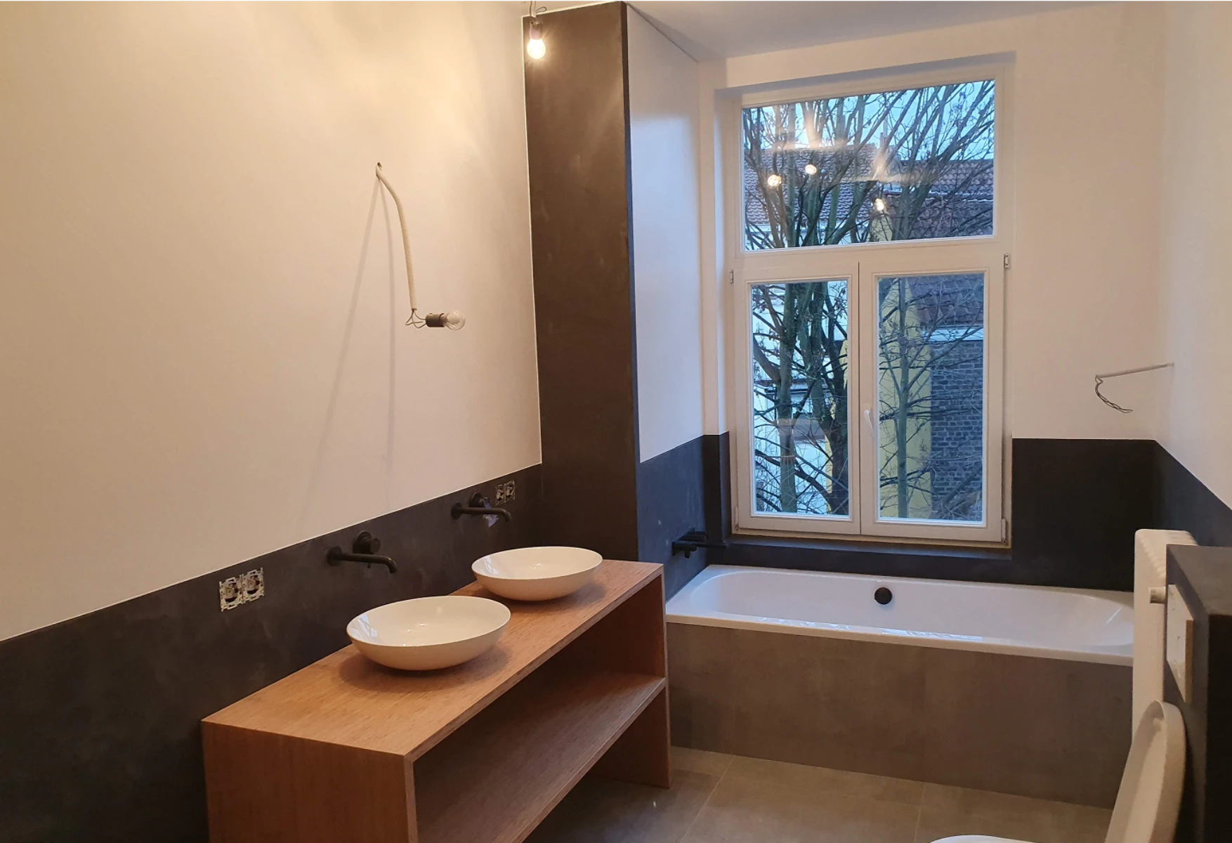 Rénovation salle de bain : vasques posées sur meuble en bois, robinets muraux, baignoire sous fenêtre et câblage électrique apparent