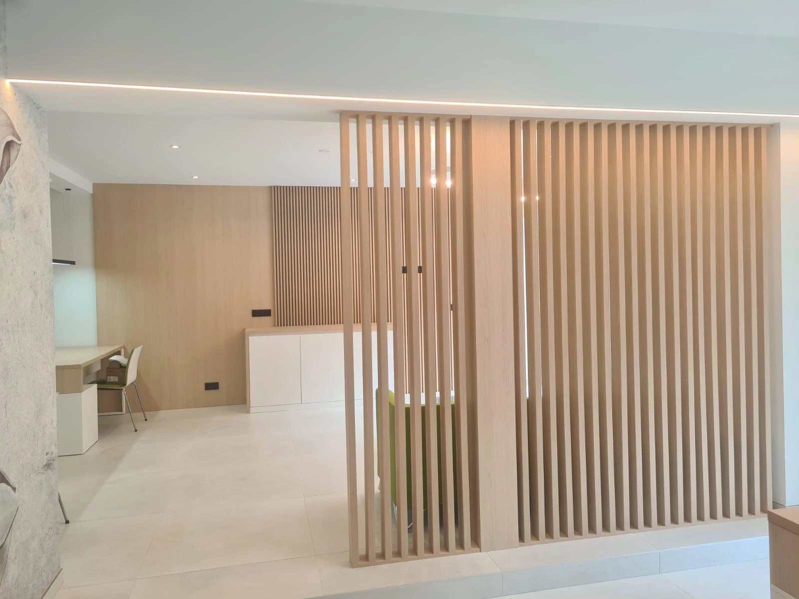 Cloison amovible en lattes de bois séparant un espace intérieur lumineux avec sol carrelé et plafond LED