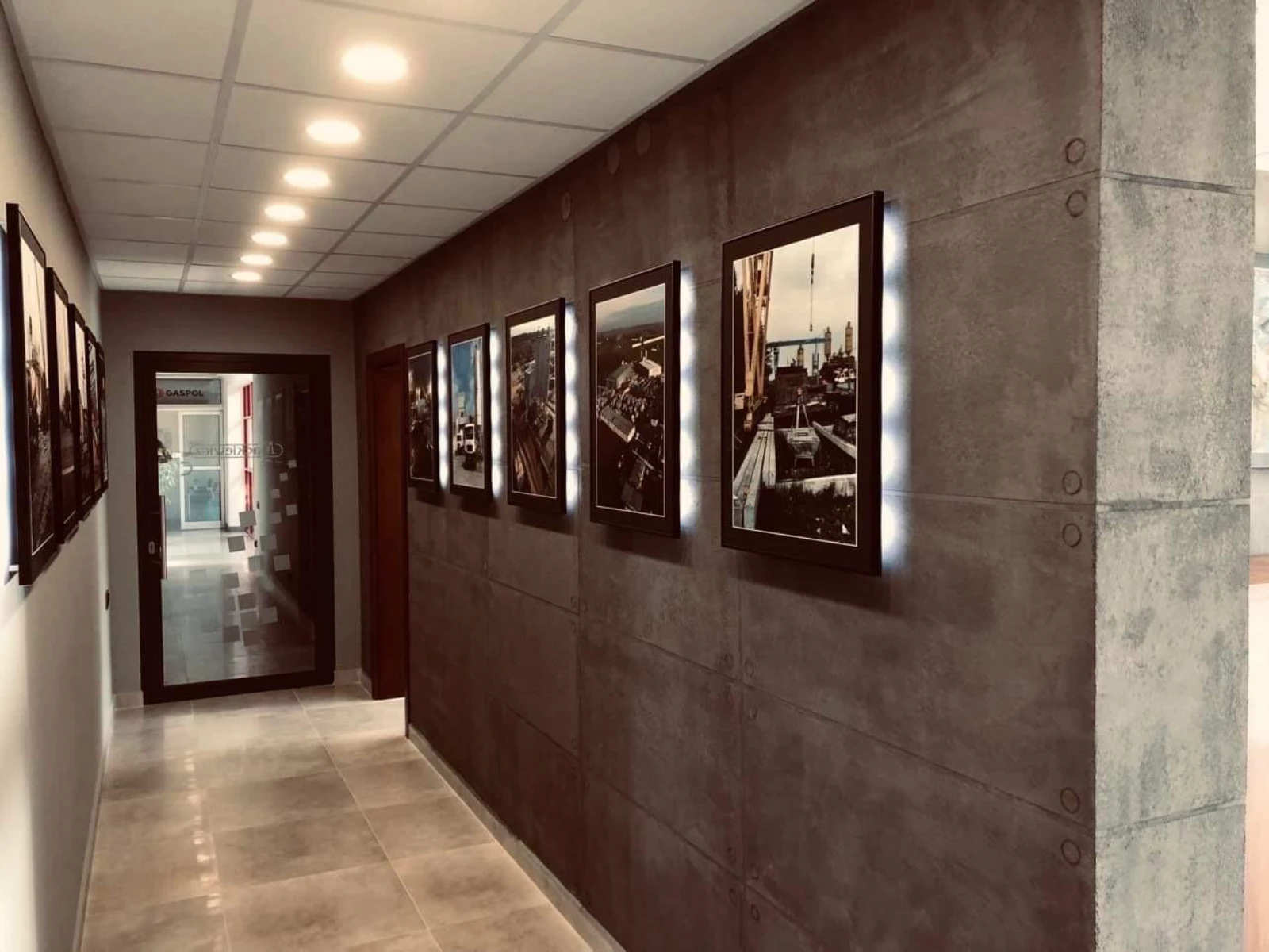 Couloir intérieur avec faux plafond et éclairage led à spots encastrés, mur sombre décoré de cadres rétroéclairés