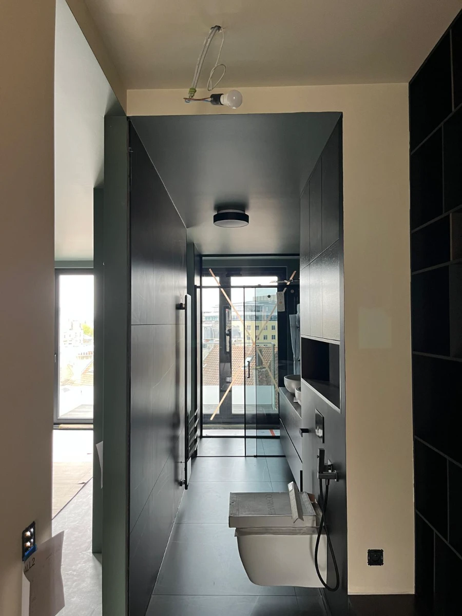 Vue d’un espace de salle de bain en cours d’aménagement avec douche vitrée, WC suspendu et branchement électrique apparent – Rénovation salle de bain