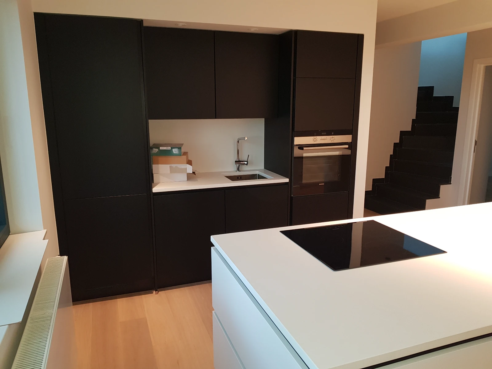 Cuisine contemporaine avec îlot blanc équipé d’une plaque à induction encastrée et meubles noirs laqués – Installation électrique