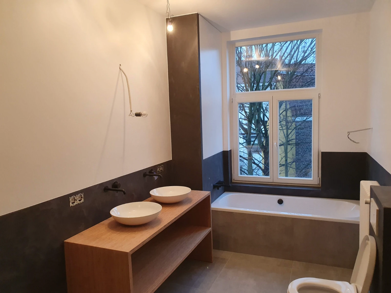 Salle de bain en cours de rénovation avec meuble vasque bois, deux vasques blanches, robinetterie noire, baignoire carrelée et câblage apparent – Rénovation salle de bain